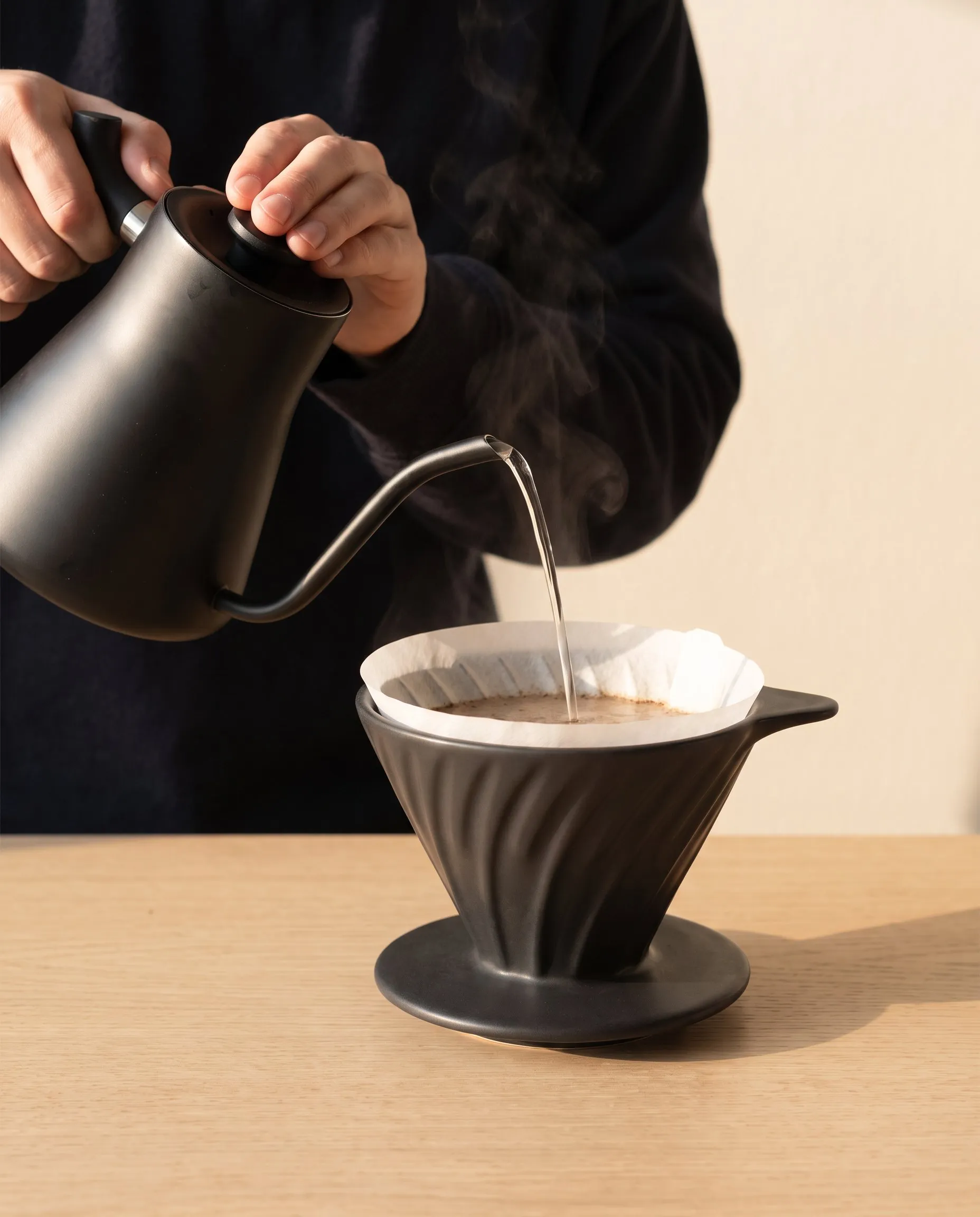 Tangan menuang air dari ketel leher angsa ke corong Bloom